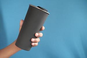 holding reusable eco coffee cup on blue background photo