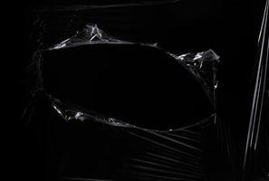 a black transparent plastic texture with hole for poster and cover art. realistic plastic wrap for overlay, copy space and photo effect. wrinkled plastic surface on black background