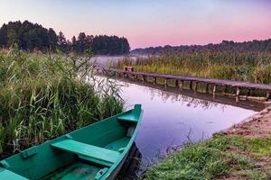 viejo barco de madera en los arbustos de caña en la orilla de un río o lago ancho foto