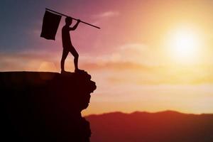 Man holding a flag standing on a cliff. Concept. Conquer the goal until it has been achieved.. photo