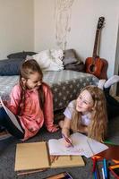 Two girls friends play at home, draw with pencils and felt-tip pens and have fun photo