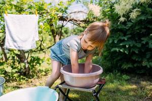 Little preschool girl helps with laundry. Child washes clothes in garden photo