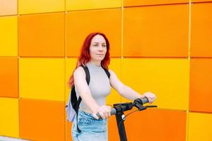 Young bright woman smiles and rides an electric scooter in the summer in city photo