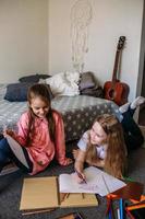 Two girls friends play at home, draw with pencils and felt-tip pens and have fun photo