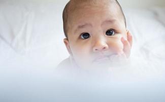 Asian cute baby in white sunny bedroom. Newborn child relaxing on bed photo