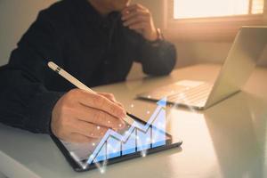 businessman working with statistics, looking at laptop and phone screens with graphs and diagrams, synchronizing electronic devices, checking financial report presentation, sitting at desk photo