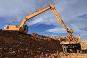 Heavy excavator loading dumper truck with sand in quarry over blue sky photo