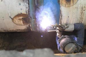 Male welder worker wearing protective clothing fixing welding   and sewerage plumbing pipeline outside on site photo