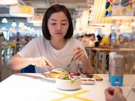 Asian woman sitting separated in restaurant eating food with table shield plastic partition to protect infection from coronavirus covid-19 photo