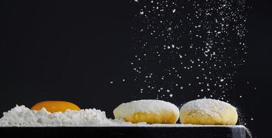 Dough and raw egg yolk on black background. Flour pours on fresh homemade dough. Bakery concept. Flour pours on the table. Photo with copy space.