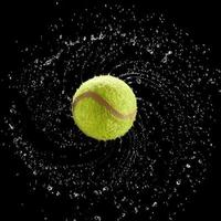 Tennis ball spinning fast splashing water drops in a circle on black background.