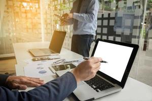 business documents on office table with smart phone and digital laptop and graph financial diagram and businessman working in the background, business concept. photo