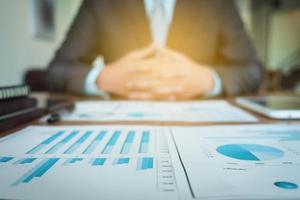 business documents on office table with graph financial diagram and businessman working in the background, business concept. photo