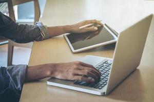 primer plano de la mano masculina, usando tableta digital y computadora mientras está sentado en su lugar de trabajo. foto