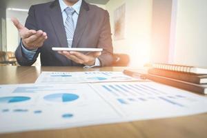 Handsome young businessman working with touchpad while sitting on the couch in office and financial statistic graph. photo