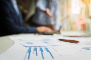 business documents on office table with laptop and digital tablet and stylus and two colleagues discussing data in blurred background. photo