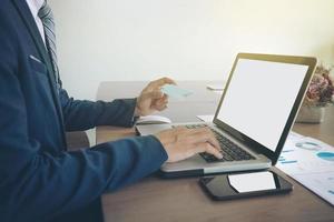 Man holding card in hand and entering security code using smart phone on laptop keyboard, online shopping concept. photo