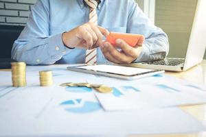 businessman using calculator with stacked coins arranged at office desk and many document data graph in morning light, business concept. photo