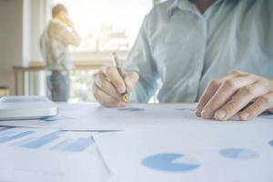 Handsome young businessman working with laptop while sitting on the desk in office and financial statistic graph photo