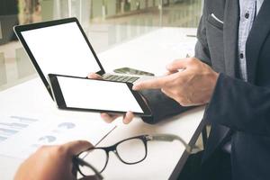 primer plano de la mano masculina, usando tableta y computadora portátil mientras está sentado en su lugar de trabajo. foto