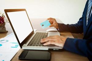 Close-up of man hands holding business card, working on laptop and smart phone in cafe with internet. photo