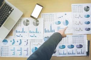 hombre de negocios señalando documentos en la mesa de trabajo de la oficina con teléfono inteligente y computadora, vista superior. foto