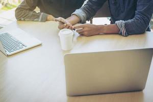 primer plano de la mano masculina, usando el teléfono y la computadora mientras está sentado en su lugar de trabajo. foto