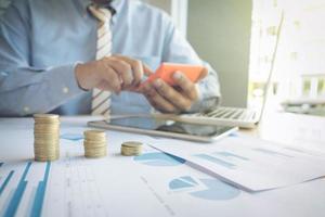 businessman using calculator with stacked coins arranged at office desk and many document data graph in morning light, business concept. photo