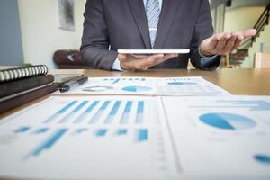 Handsome young man working with touchpad while sitting on the couch in office and financial statistic graph photo