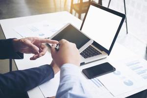 business documents on office table with smart phone and digital laptop and graph financial diagram and businessman working in the background. photo