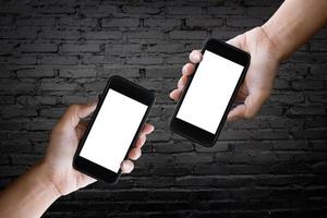 dos manos sosteniendo la pantalla en blanco de un teléfono inteligente en la vieja pared de ladrillo negro. foto