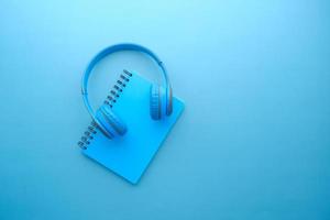 Audio book concept. Headphones and notepad on blue background photo