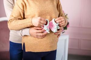 knitted booties in the hands of a pregnant woman next to her husband. waiting for a miracle photo