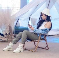Portrait beautiful young girl woman Asian pretty smile one person alone sitting on chair camping with using tablet connected the Internet to work. travel trip in front tent freedom relax happy enjoy photo