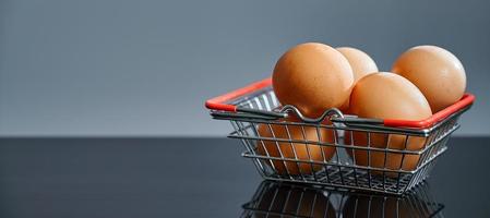 Eggs in the shopping basket on a black table with a reflection. Brown eggs in the basket. Photo with copy space.