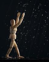 Wooden mannequin of a man in the rain pulls his hands up on a black background. The concept of joy. A wooden figure walks through puddles. photo