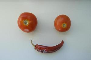 tomates orgánicos maduros rojos y pimiento rojo picante seco en el alféizar de la ventana en forma de carita sonriente y emoji foto