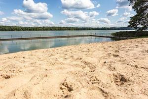 pier on sand shore of a large lake in summer day with beautiful clouds.  sky reflection photo