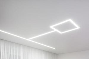 looking up on suspended ceiling with halogen spots lamps and drywall construction in empty room in apartment or house. Stretch ceiling white and complex shape. photo