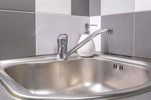 Soap and shampoo dispensers near Ceramic Water tap sink with faucet in expensive kitchen photo