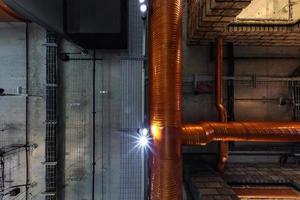 mirando hacia el techo de hormigón gris con manchas halógenas y lámparas edison en la sala de oficinas de loft con aire acondicionado y tubería de ventilación naranja foto