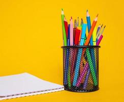 lápices de colores en una caja de lápices sobre un fondo amarillo con una hoja de papel blanca foto