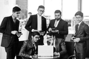 grupo de seis hombres de negocios indios en trajes sentados en la oficina en el café mirando la computadora portátil y tomando café. foto