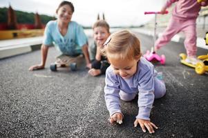 cuatro niños en asfalto juegan y se divierten. la familia deportiva pasa tiempo libre al aire libre con scooters y patines. foto