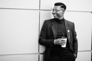 Amazingly looking african american man wear at blue blazer with brooch, black turtleneck and glasses posed at street. Fashionable black guy with cup of coffee. photo