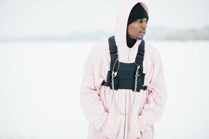 Elegante hombre afroamericano de estilo urbano con capucha rosa posado en un lago congelado en invierno. foto