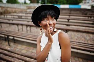 Amazing african american model woman in green pants and black hat posed at bench. photo