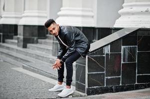 Stylish indian beard man at black leather jacket. India model posed sitting at streets of city. photo