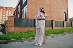 hombre de negocios árabe del medio oriente posó en la calle contra un edificio moderno con gafas de sol, hablando por teléfono móvil. foto