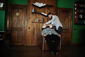 apuesto hombre barbudo en la barbería, peluquero en el trabajo. cabezal de lavado. foto